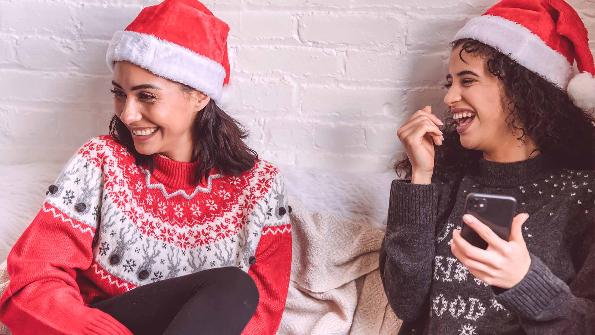 girls laughing dressed up in holiday sweaters and santa hats